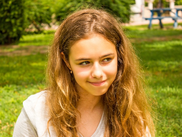 Schönes jugendlich Mädchen mit dem langen Haar lächelnd im Park auf dem grünen Gras