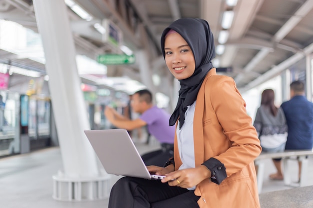 Schönes junges asiatisches Mädchen, das an einem skytrain mit einem Laptop arbeitet. Muslimische Frauen