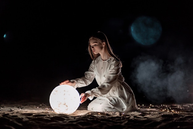 Schönes junges attraktives Mädchen an einem Nachtstrand mit Sand und Sternen hält den Mond in ihren Händen