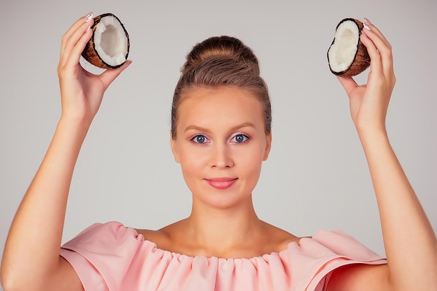 Schönes junges blondes Frisurmädchen mit Kokosnuss in ihrer Hand schultern nackt nackt im Studio auf einem weißen Hintergrund. Schönheit von Haaren und Haut.