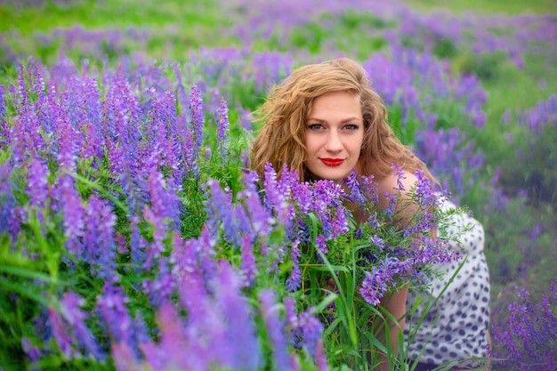 Schönes junges blondes Mädchen in einem grünen Feld unter lila Wildblumen. Schönes Mädchen der Tierwelt.