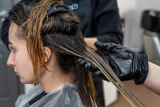 Schönes junges brünettes Mädchen, das beim besten Meister auf dem Verfahren der Haarfärbung sitzt