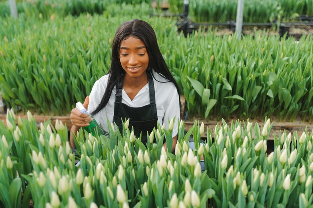 Schönes junges lächelndes Afroamerikanermädchen, Arbeiter mit Blumen im Gewächshaus.