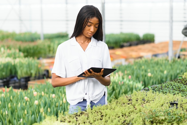 Schönes junges lächelndes Afroamerikanermädchen, Arbeiter mit Blumen im Gewächshaus.