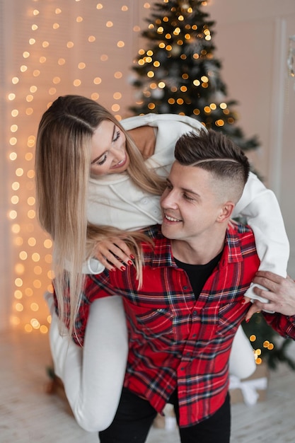 Schönes junges lebenslustiges Paar in modischer Kleidung hat Spaß und Spaß vor einem Weihnachtsbaum und Lichtern