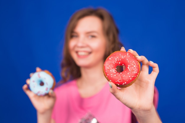 Schönes junges lustiges Mädchen mit Donuts auf Blau.