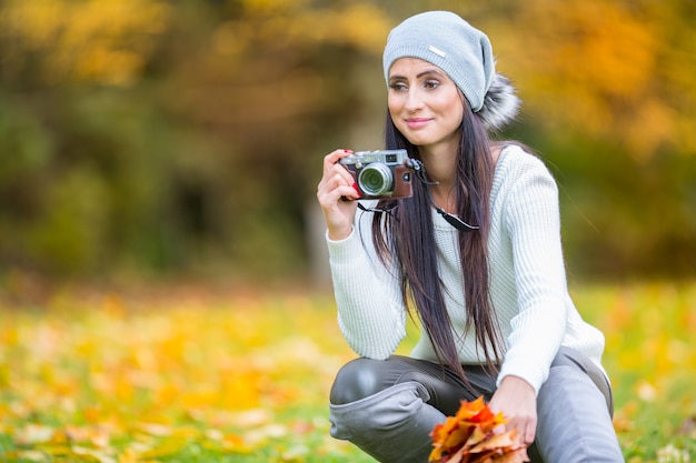 Schönes junges Mädchen, das am sonnigen Tag des Herbstes mit Retro-Kamera schießt