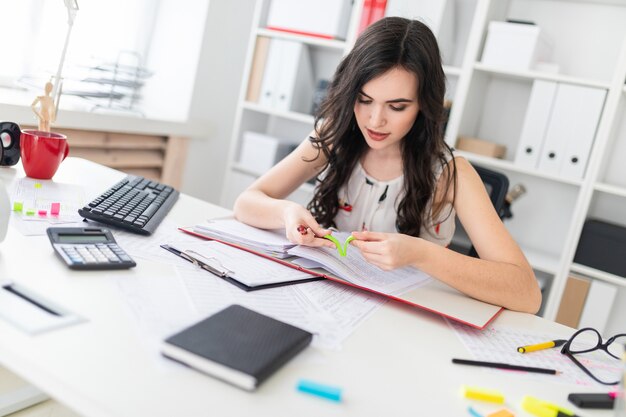 Schönes junges Mädchen, das an einem Schreibtisch hält einen Stift in ihrer Hand und reißt einen hellen Aufkleber ab sitzt.