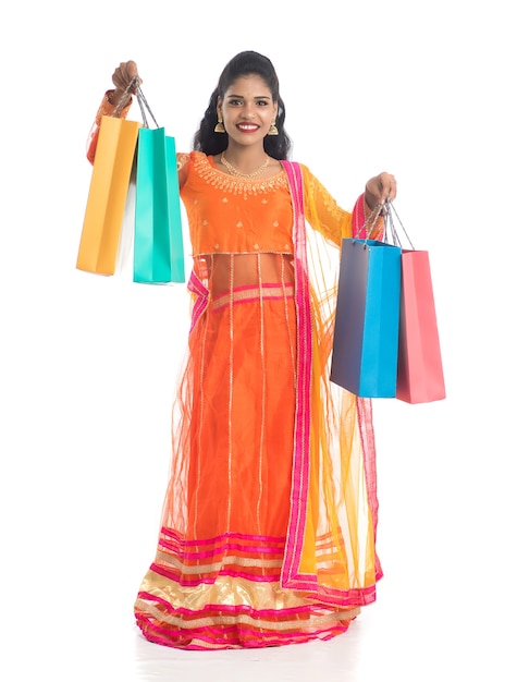 Schönes junges Mädchen, das Einkaufstaschen beim Tragen der traditionellen ethnischen Abnutzung auf Weiß hält