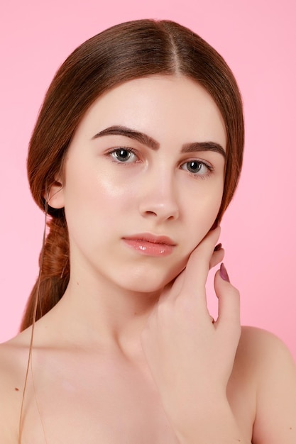 Schönes junges Mädchen, das ihre perfekte Haut auf rosa Hintergrund berührt. Hautpflegekonzept. Schönheits-Frauen-Porträt mit sauberer Haut. Süßes Mode-Modell der Schönheit mit natürlichem Make-up auf rosa Hintergrund