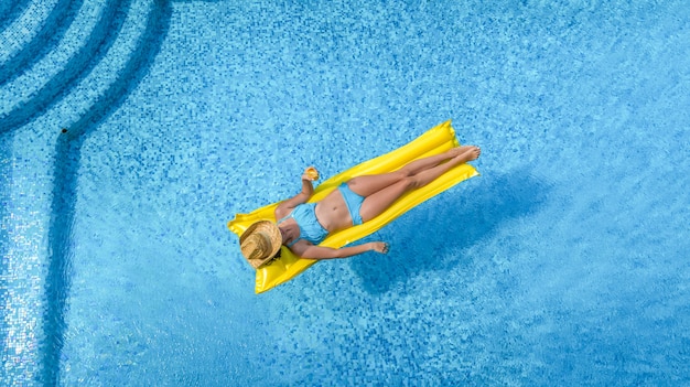 Schönes junges Mädchen, das im Schwimmbad entspannt, Frau schwimmt auf aufblasbarer Matratze und hat Spaß im Wasser im Familienurlaub, tropischem Ferienort, Luftdrohnenansicht von oben