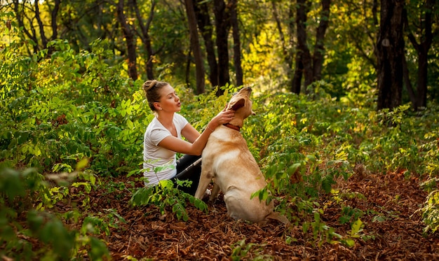 schönes junges Mädchen, das im Wald mit einem Hund sitzt und ihr geliebtes Haustier streichelt