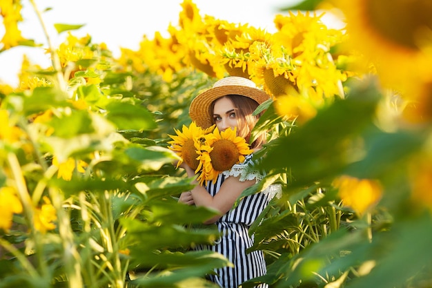 Schönes junges Mädchen, das Natur auf dem Feld der Sonnenblumen am Sonnenuntergang genießt