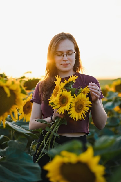 Schönes junges Mädchen, das Natur auf dem Feld der Sonnenblumen am Sonnenuntergang genießt