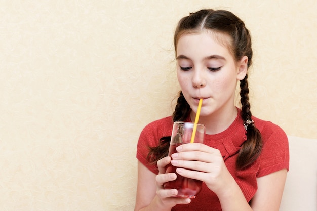 Foto schönes junges mädchen, das saft durch einen strohhalm zu hause trinkt