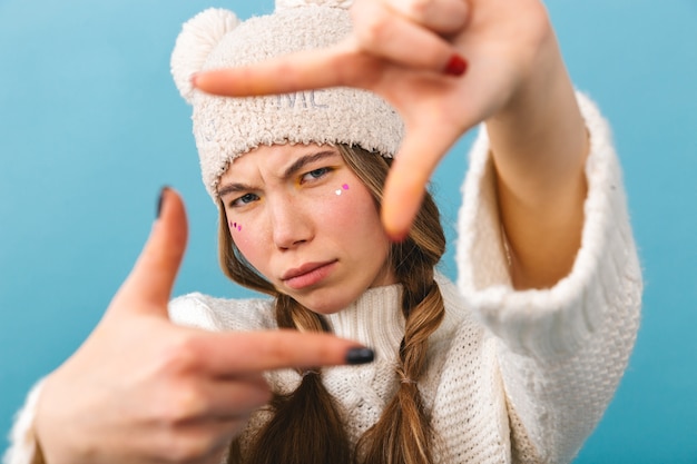 Schönes junges Mädchen, das Winterkleidung trägt, die lokal steht und Rahmengeste mit Händen zeigt