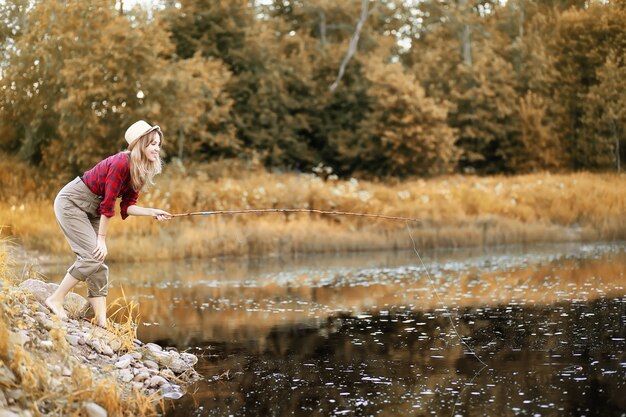 Schönes junges Mädchen im Herbst am Fluss mit einer Angelrute