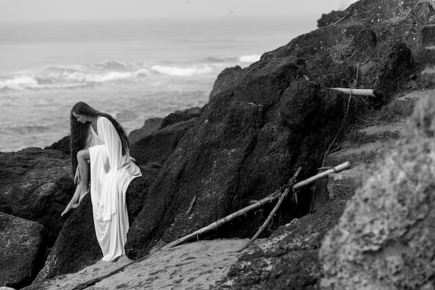 Schönes junges Mädchen im Hochzeitskleid und am schwarzen Strand in Varkala, Kerala mit hohem Felsen