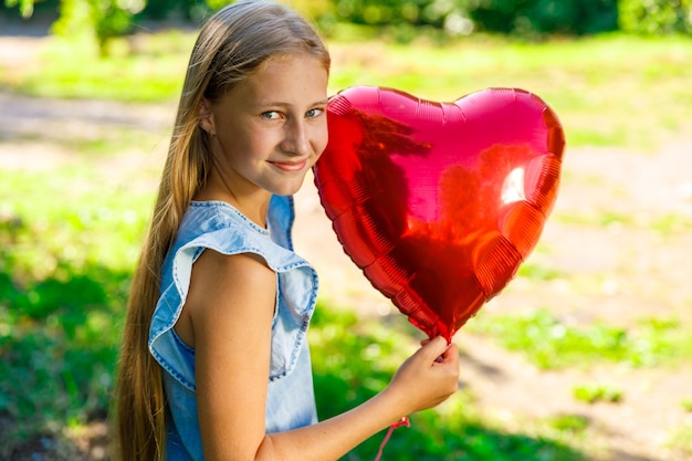 Schönes junges Mädchen in einem blauen Kleid mit einem herzförmigen Ballon