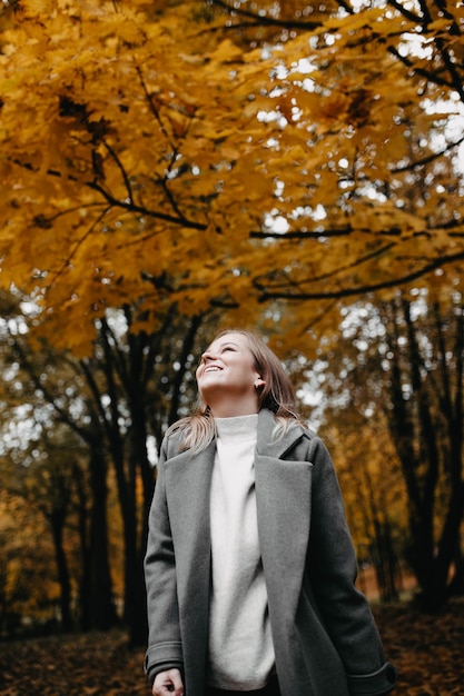 schönes junges Mädchen in einem Herbstpark in einem grauen Mantel posiert für ein Fotoshooting in der Natur