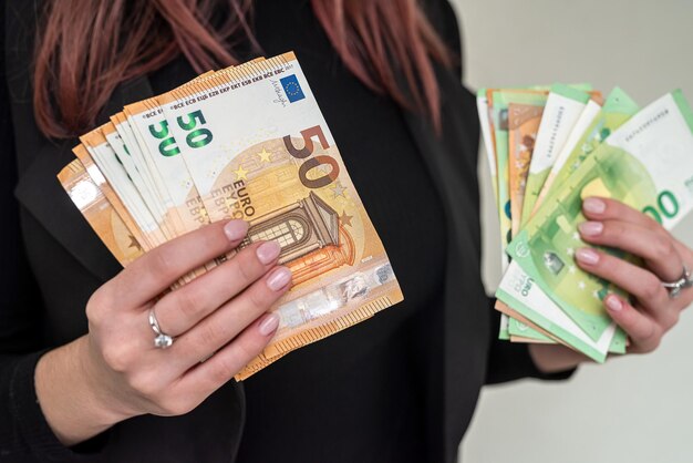 Schönes junges Mädchen in einem stilvollen schwarzen Anzug hält eine große Summe neuer Euros in seinen Händen