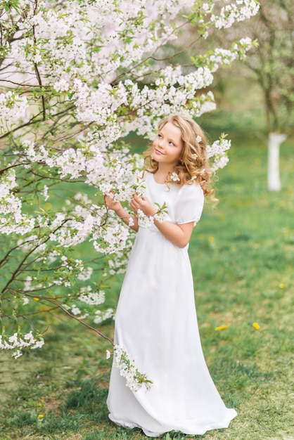 Schönes junges Mädchen in einem weißen langen Kleid in einem blühenden Frühlingsgarten