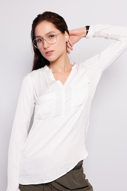 Foto schönes junges mädchen in weißem t-shirt mit brille, leere wand-studio-porträt, lächelnde brünette frau mit brille