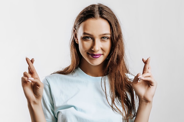 Schönes junges Mädchen lächelt gekreuzte Finger für Glück auf einem weißen isolierten Hintergrund