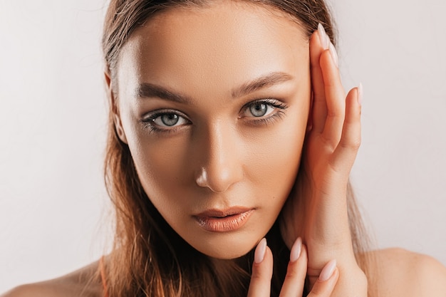 Schönes junges Mädchen lächelt und posiert in die Kamera schaut auf einem weißen isolierten Hintergrund mit Modell. Positive Brunettefrau. Freundlicher Blick. Schönheitsgesicht