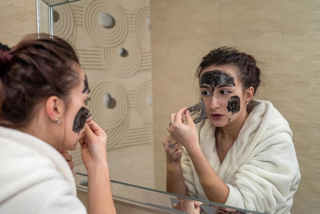 Schönes junges Mädchen macht eine schwarze Maske für Akne im Gesicht Akne-Maskenkonzept