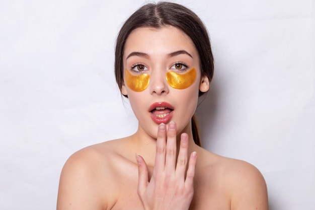 Schönes junges Mädchen mit Augenklappen. Lifting-Anti-Falten-Maske unter den Augen. Frau mit perfekter sauberer frischer Haut. Collagen-Hydrogel-Pflaster von Gold Cosmetics. Hautpflege, Gesichtsbehandlungskonzept.