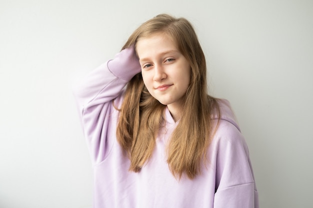 Schönes junges Mädchen mit langen Haaren im lila huddy, das gegen weiße Wand steht.