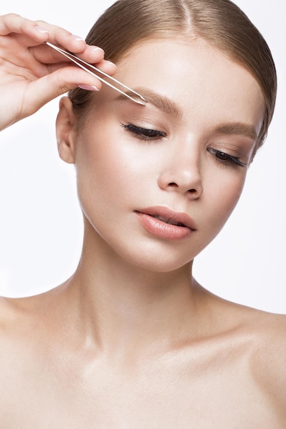 Schönes junges Mädchen mit leichtem Natur-Make-up, Augenbrauenpinzette und French Manicure. Schönheitsgesicht. Aufnahme im Studio auf weißem Hintergrund.