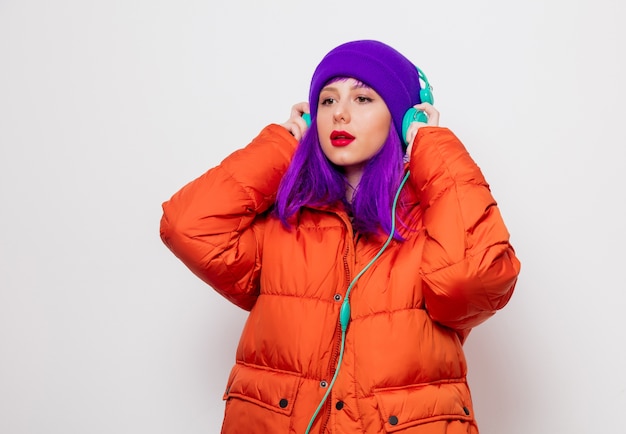 Schönes junges Mädchen mit lila Haaren und in orangefarbener Jacke hören Musik in Kopfhörern.