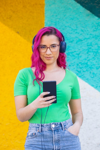 Schönes junges Mädchen mit rosa Haaren und Brille, das Musik über Kopfhörer Street Style Colo hört