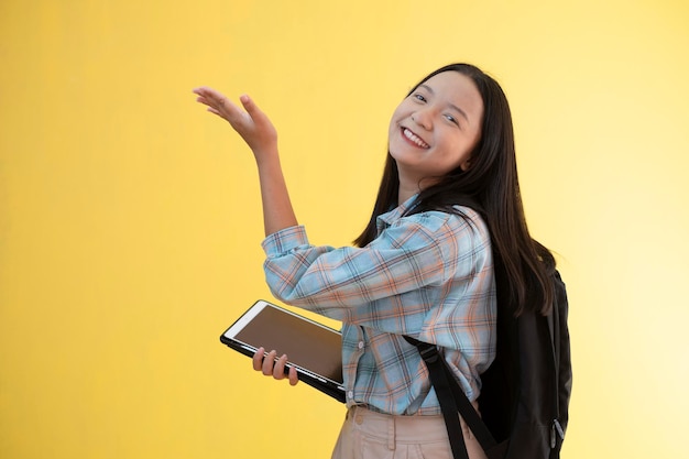 Schönes junges Mädchen mit Rucksack und Laptop auf gelbem Hintergrund.