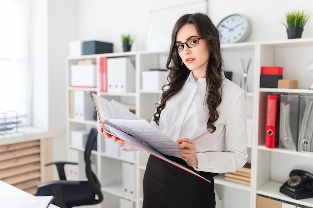 Schönes junges Mädchen steht im Büro Daumen einen Ordner mit Dokumenten.