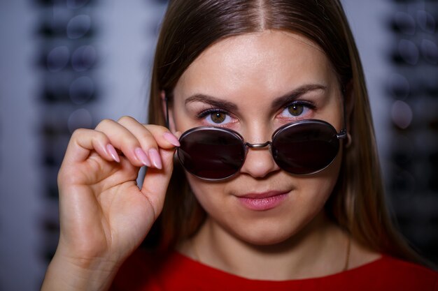 Schönes junges Mädchen wählt Sonnenbrille in einem Optikgeschäft.