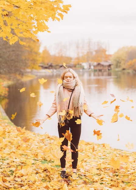 Schönes junges Mädchen wirft Herbstlaub. Attraktive junge Frau steht still und täuscht herum