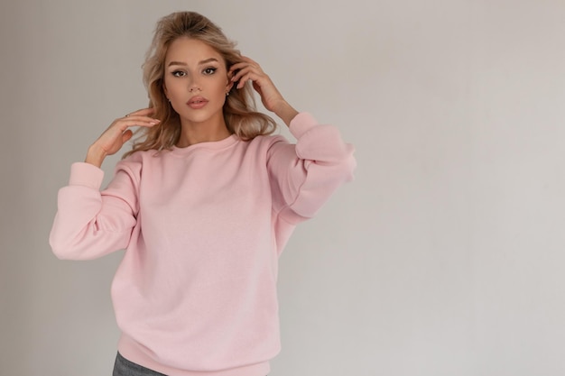 Schönes junges Mädchenmodell mit blonden Haaren in einem modischen rosa Pullover auf grauem Hintergrund im Studio Kopieren Sie Platz für Design