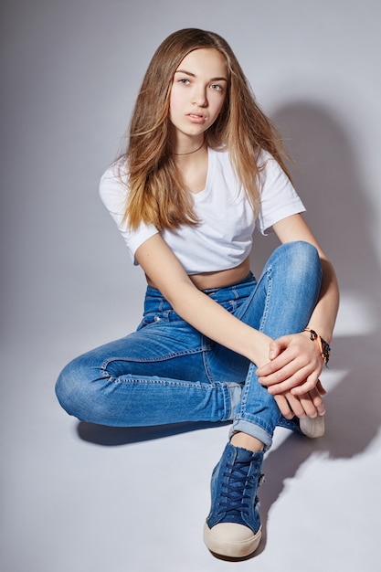 Foto schönes junges mode-modell-mädchen in den blue jeans, die auf dem boden sitzen