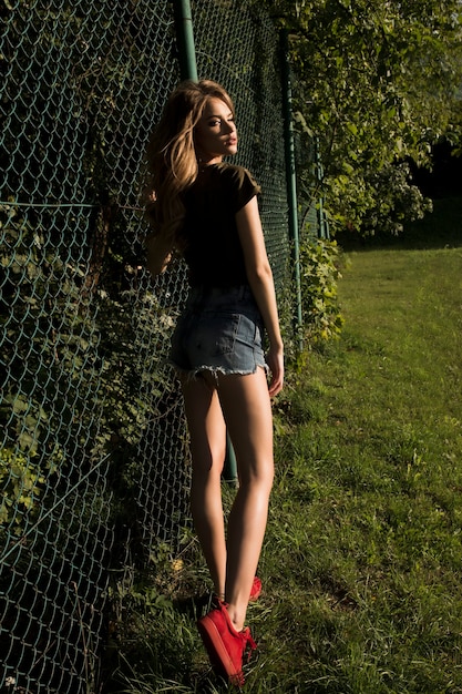Schönes junges Model posiert am Gitterzaun in stilvoller Kleidung