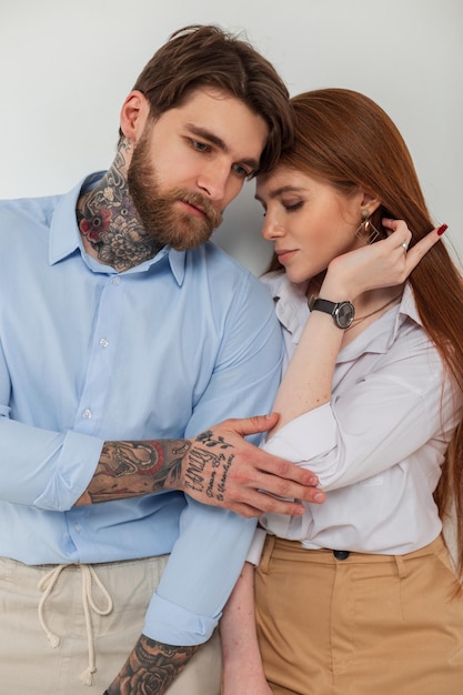 Schönes junges Modepaar Brutaler trendiger Hipster-Mann mit Tattoo und Bart und hübsche junge rothaarige Frau mit eleganter Modekleidung auf weißem Hintergrund