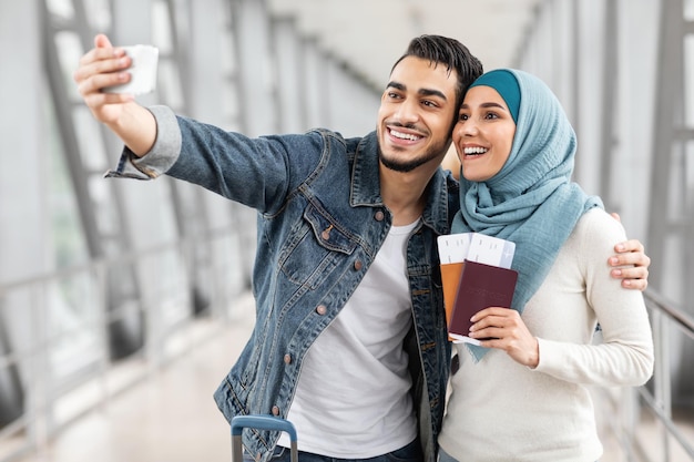 Schönes junges muslimisches Paar, das am Flughafen ein Selfie mit dem Smartphone macht