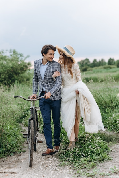 Schönes junges Paar Braut und Bräutigam, die in einem Feld mit einem Fahrrad gehen