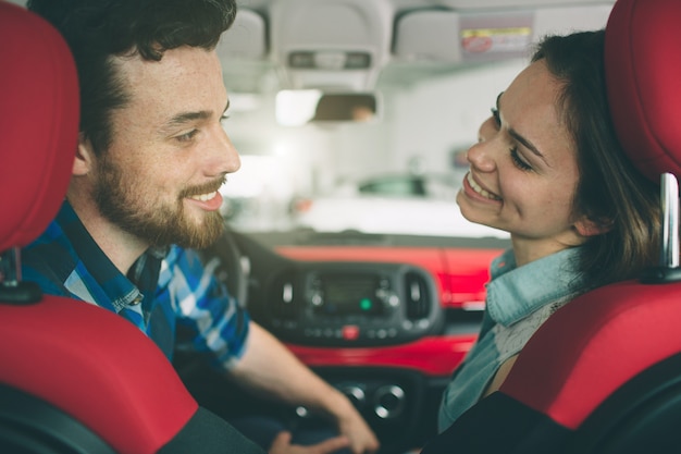 Schönes junges Paar, das am Autohaus steht und das Auto wählt, um zu kaufen