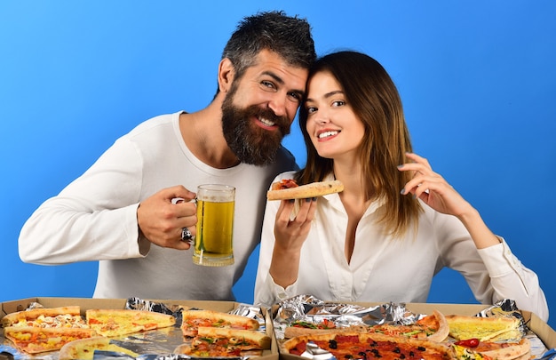 Schönes junges Paar, das Bier trinkt und Pizza isst. Modernes Paar, das zu Hause Pizza isst und eine tolle Zeit zusammen hat. Konsum, Essen und Trinken, Menschenkonzept - glückliche Freunde, die Pizza essen, Getränke be