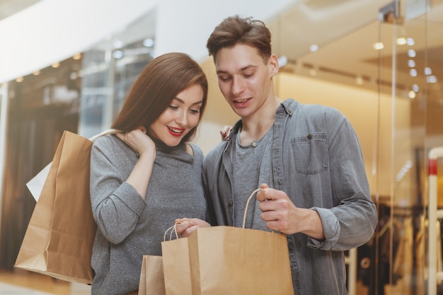 Schönes junges Paar, das ihren Kauf prüft und in Einkaufstaschen schaut
