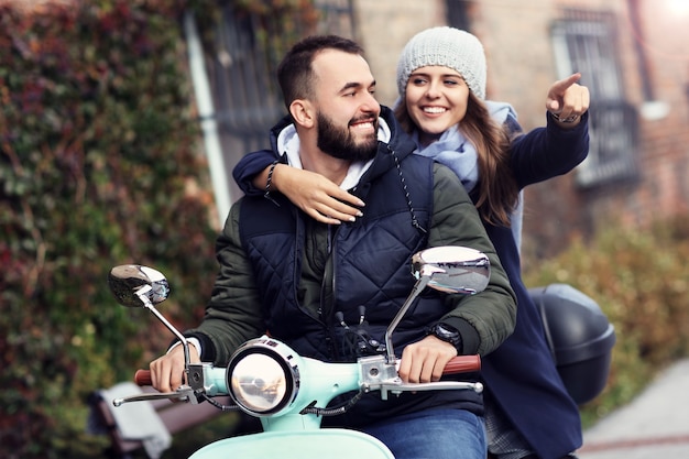 Schönes junges Paar, das im Herbst beim Rollerfahren in der Stadt lächelt