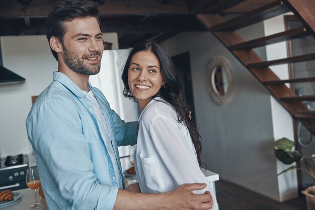 Schönes junges Paar, das lächelt und sich verbindet, während es Zeit in der Küche verbringt